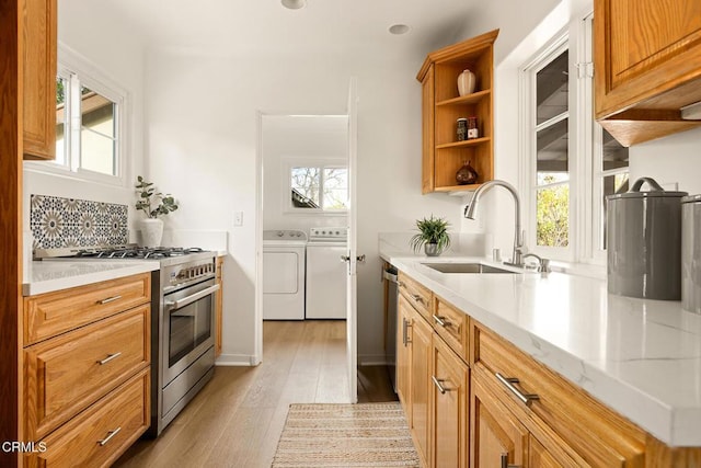 kitchen featuring a sink, washer and clothes dryer, light wood-style floors, stainless steel appliances, and open shelves