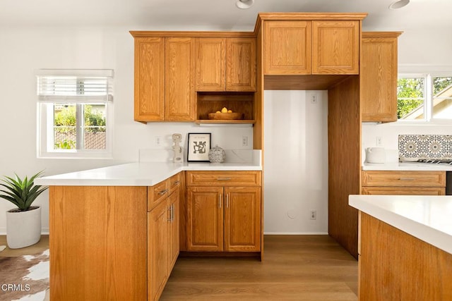 kitchen featuring a peninsula, brown cabinetry, light wood finished floors, decorative backsplash, and light countertops