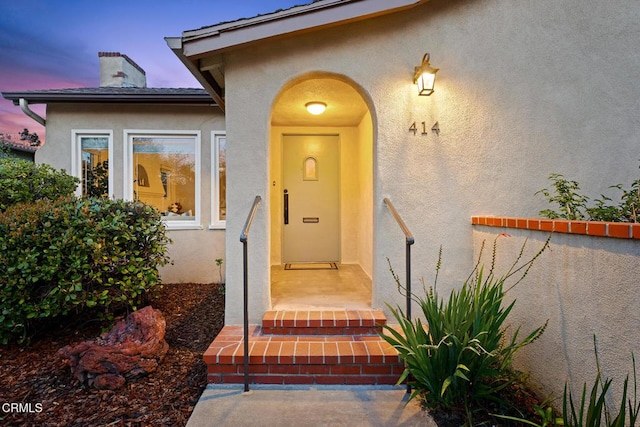 view of exterior entry with stucco siding and a chimney