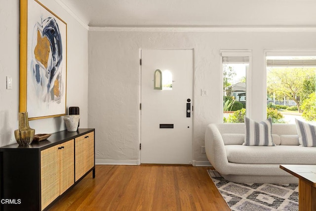 foyer entrance featuring ornamental molding, baseboards, a textured wall, and wood finished floors