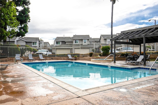 pool with a patio, a community hot tub, fence, and a residential view