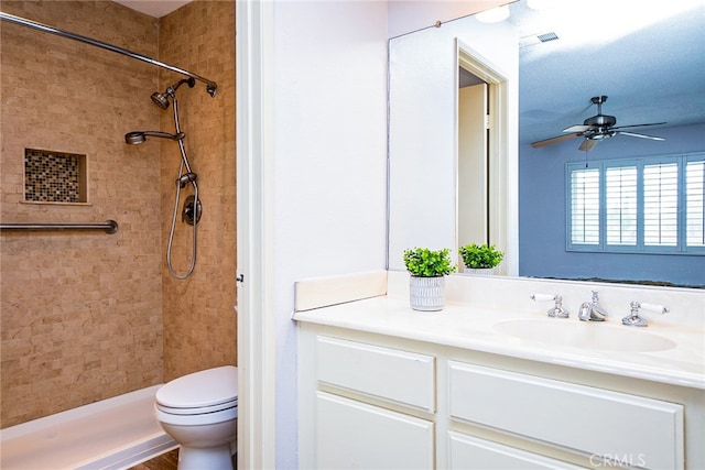 full bathroom with vanity, a ceiling fan, visible vents, tiled shower, and toilet