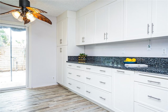 kitchen with a ceiling fan, dark stone countertops, a textured ceiling, light wood-style floors, and white cabinets