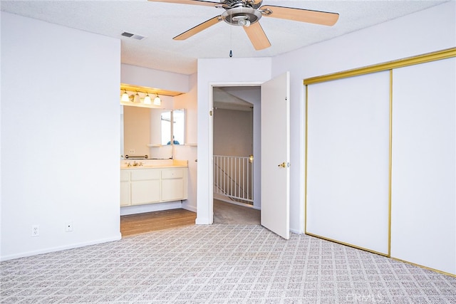 unfurnished bedroom featuring visible vents, ensuite bath, a sink, a closet, and light carpet