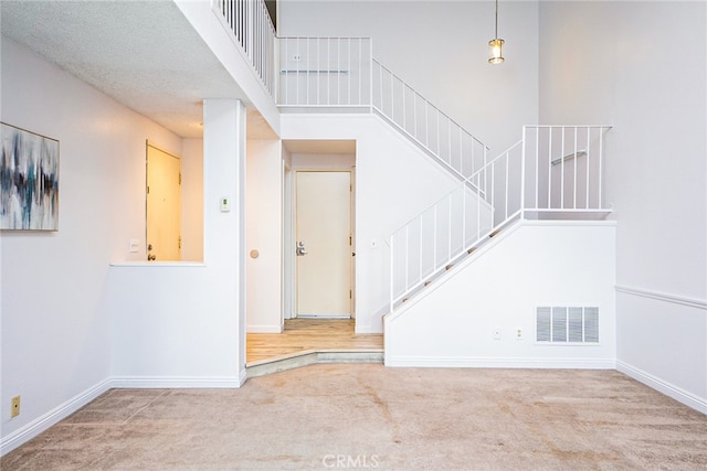 stairs with carpet, visible vents, a towering ceiling, and baseboards