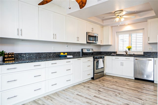 kitchen featuring ceiling fan, a tray ceiling, light wood-style flooring, appliances with stainless steel finishes, and white cabinets