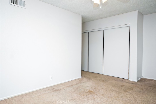 unfurnished bedroom with visible vents, carpet floors, a textured ceiling, and a closet