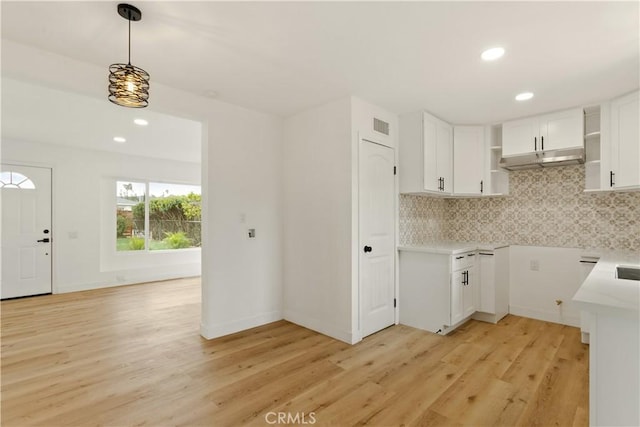 kitchen with under cabinet range hood, decorative backsplash, light wood-style floors, and white cabinetry