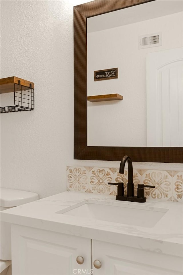 half bathroom featuring visible vents, toilet, vanity, and a textured wall