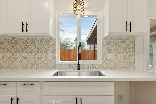 kitchen with light stone counters, white cabinetry, and a sink