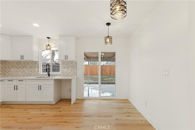 kitchen with tasteful backsplash, light countertops, light wood-style flooring, white cabinets, and a sink