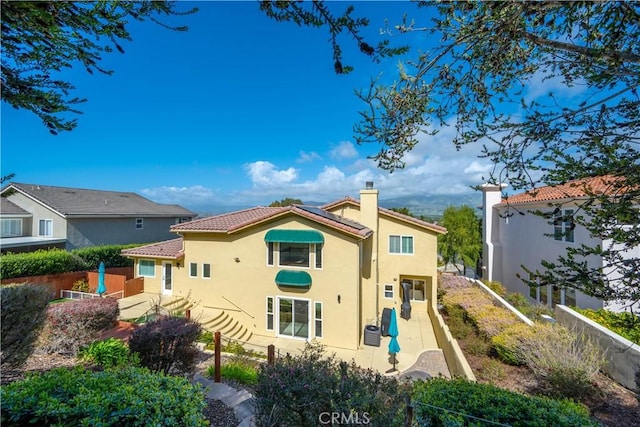 rear view of property featuring stucco siding, a tiled roof, fence, and a chimney