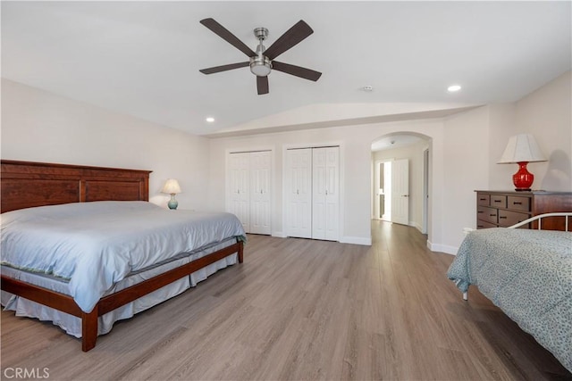 bedroom with light wood finished floors, baseboards, multiple closets, vaulted ceiling, and arched walkways