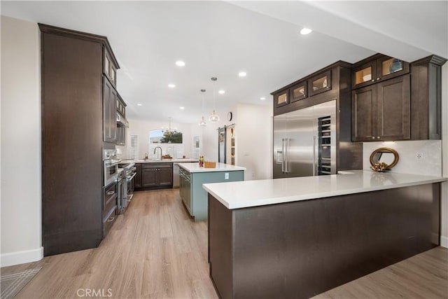 kitchen featuring dark brown cabinets, built in refrigerator, light countertops, a peninsula, and a sink