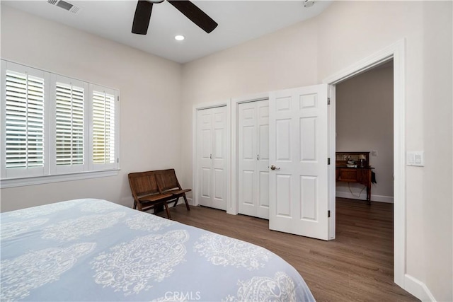 bedroom with visible vents, ceiling fan, baseboards, multiple closets, and wood finished floors