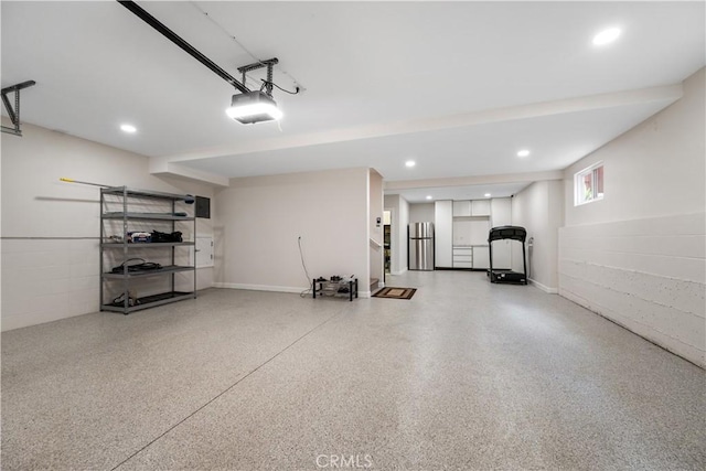 garage featuring freestanding refrigerator, recessed lighting, concrete block wall, and a garage door opener