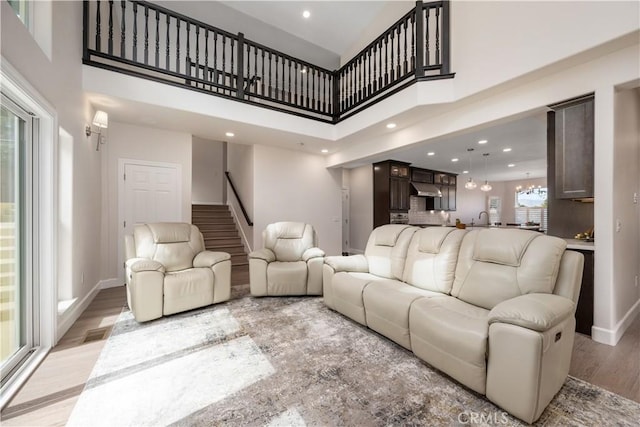 living room featuring visible vents, baseboards, an inviting chandelier, stairs, and light wood-style floors