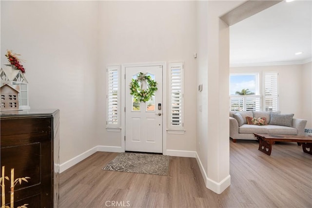 foyer with crown molding, baseboards, and light wood finished floors