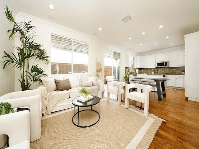 living room with visible vents, recessed lighting, light wood-type flooring, and ornamental molding