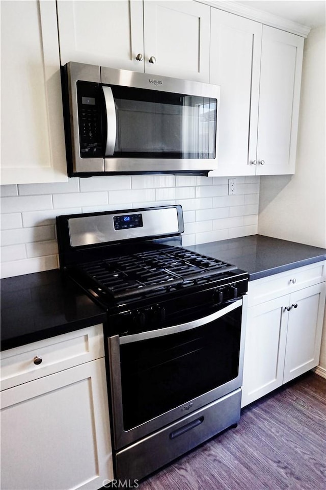 kitchen featuring dark countertops, dark wood-type flooring, decorative backsplash, appliances with stainless steel finishes, and white cabinetry