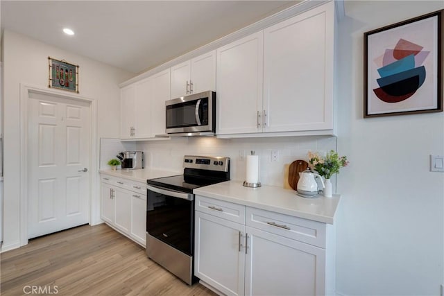 kitchen featuring light countertops, appliances with stainless steel finishes, white cabinetry, light wood-type flooring, and backsplash