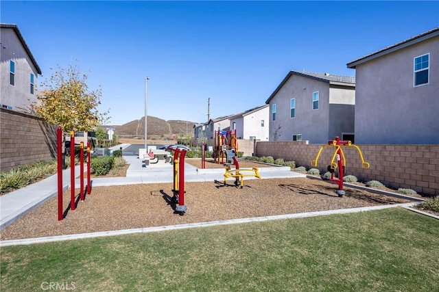 view of playground featuring a lawn, a mountain view, and fence