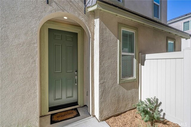 doorway to property with stucco siding and fence