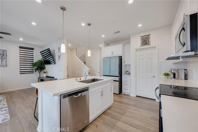 kitchen featuring visible vents, a sink, white cabinets, stainless steel appliances, and a kitchen island with sink