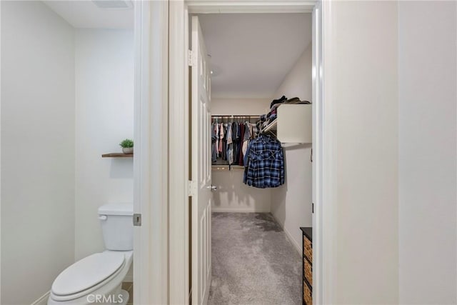 bathroom featuring a spacious closet, toilet, and baseboards