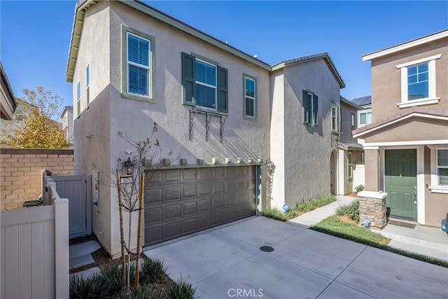 view of front of house featuring stucco siding, a garage, concrete driveway, and fence