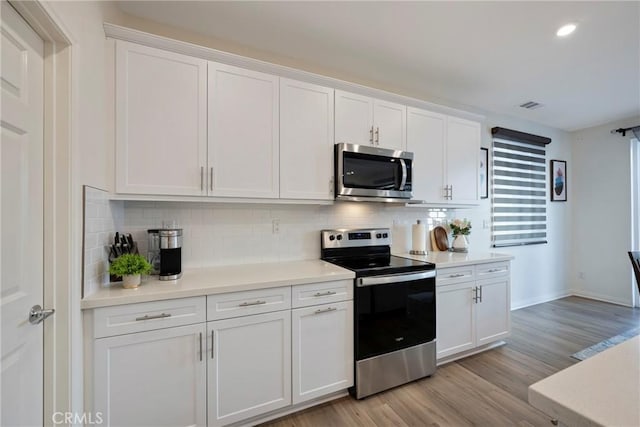 kitchen with visible vents, light wood-style flooring, decorative backsplash, appliances with stainless steel finishes, and white cabinetry