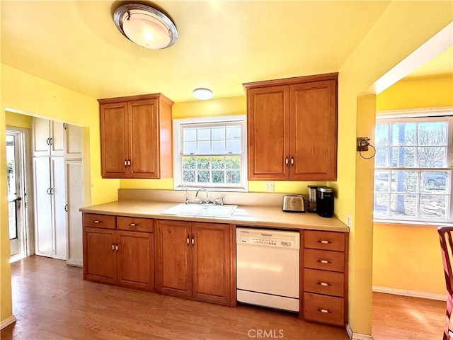 kitchen featuring a sink, brown cabinetry, white dishwasher, and light countertops