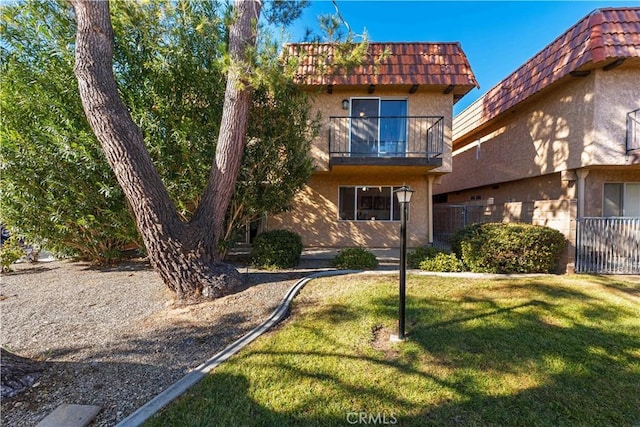 view of front facade with stucco siding, a balcony, a front lawn, and a tiled roof