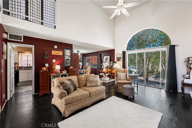 living area featuring a towering ceiling, visible vents, dark wood-style floors, and a ceiling fan