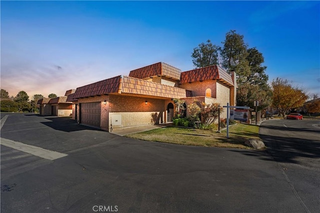 view of front facade with an attached garage, mansard roof, driveway, and stucco siding