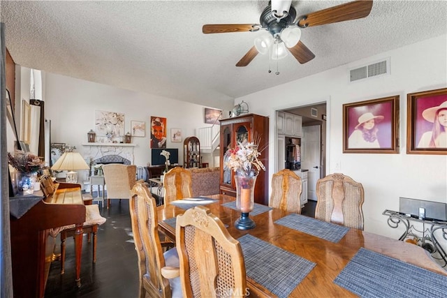 dining room with visible vents, a ceiling fan, a textured ceiling, wood finished floors, and a stone fireplace