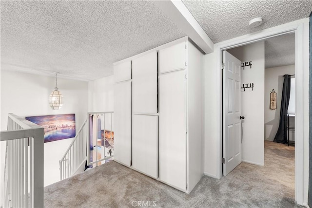 corridor featuring an upstairs landing, light colored carpet, and a textured ceiling