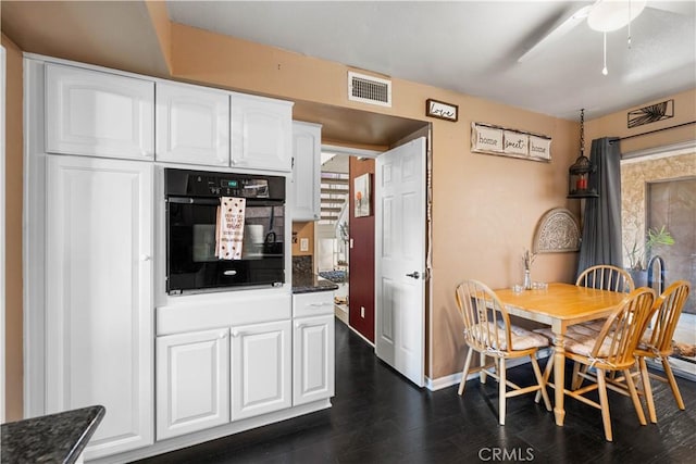 kitchen with baseboards, visible vents, dark wood-type flooring, white cabinetry, and black oven