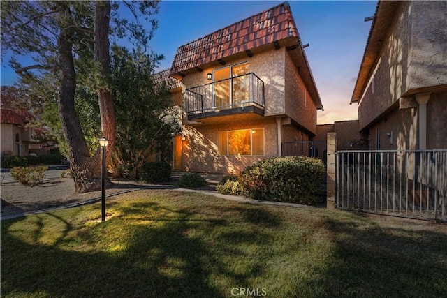 view of front of property with a front yard, a balcony, fence, mansard roof, and stucco siding