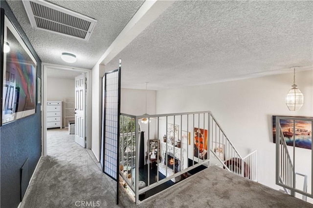 corridor with visible vents, carpet floors, a textured ceiling, and an upstairs landing