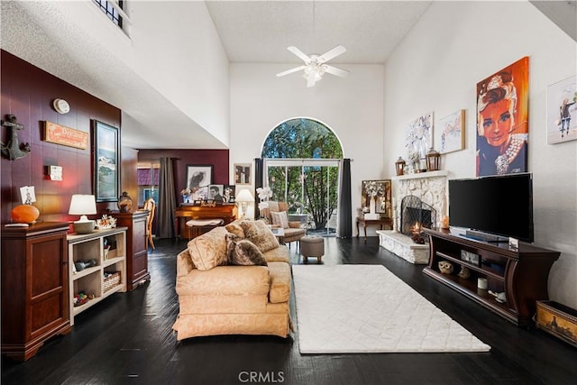 living area featuring a towering ceiling, dark wood finished floors, a fireplace, and ceiling fan