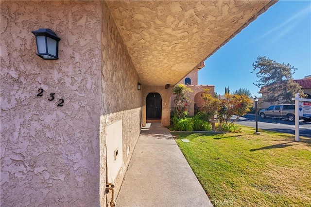 view of exterior entry featuring stucco siding and a lawn