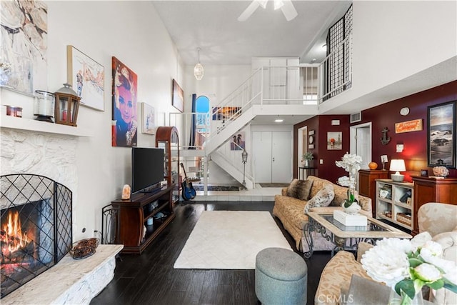 living room featuring visible vents, stairs, a fireplace, a high ceiling, and wood finished floors