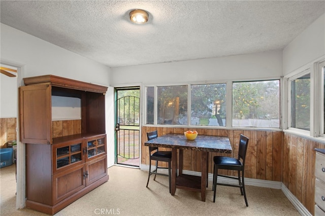 dining space featuring light carpet, wood walls, a textured ceiling, and breakfast area