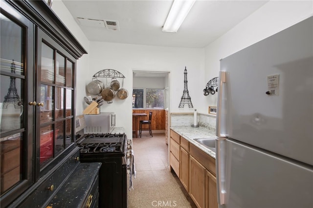 kitchen with visible vents, stainless steel range with gas cooktop, light floors, light stone counters, and freestanding refrigerator