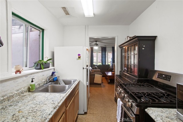 kitchen with brown cabinetry, light floors, freestanding refrigerator, a sink, and stainless steel gas stove