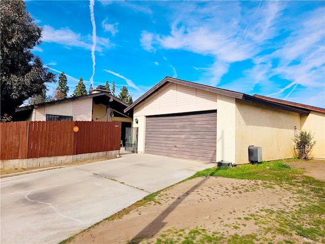 view of home's exterior with stucco siding, driveway, an attached garage, and fence