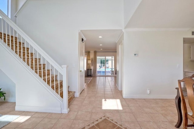 foyer entrance featuring crown molding, a high ceiling, light tile patterned flooring, and baseboards