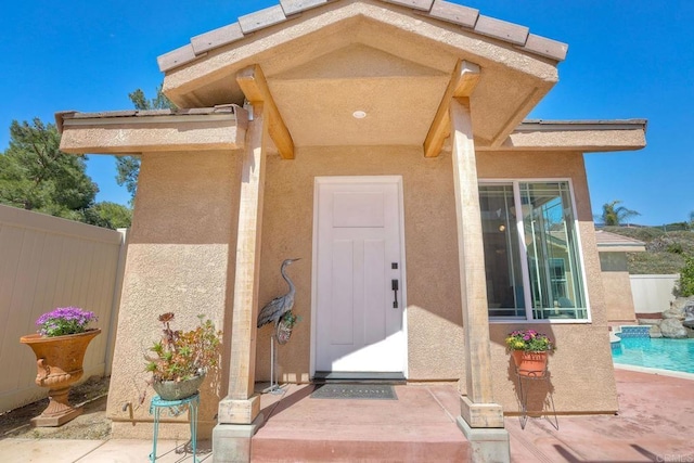 property entrance featuring stucco siding, a fenced in pool, and fence