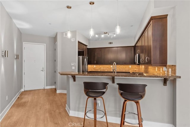 kitchen featuring dark stone countertops, dark brown cabinets, appliances with stainless steel finishes, a kitchen breakfast bar, and backsplash